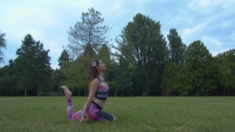 Mujer-Joven-Practicando-Yoga-En-El-Césped-Del-Parque-Público-Haciendo-Posición-De-Paloma-Rey,-Cámara-Lenta