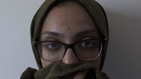 Muslimische-Frau-Mit-Brille,-Die-Hijab-Hält-Und-Ihren-Mund-Bedeckt,-Der-In-Die-Kamera-Schaut