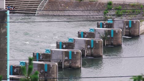 A-Couple-Of-Friends-Sitting-On-The-Riverside-Watching-The-Tamagawa-River-With-Flood-Gates-In-Tokyo,-Japan