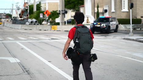 Young-black-photographer-walking-past-police-car-on-empty-road-during-Black-Lives-Matter-protest