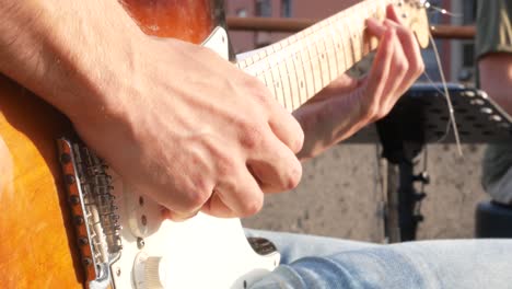 Primer-Plano-De-Un-Joven-Guitarrista-Tocando-La-Guitarra-Eléctrica-En-Un-Concierto-Al-Aire-Libre-El-Día-De-La-Música,-Con-El-Baterista-De-Fondo