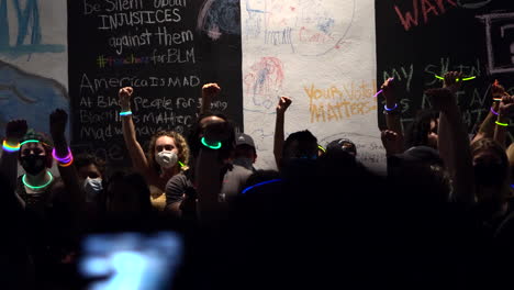 Crowd-of-protestors-raising-fists-while-holding-colorful-glowsticks-at-Chalk-the-Block-protest-at-night