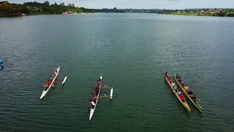 Aerial-orbit-left-view-above-colourful-teams-of-athletes-in-long-rowing-boats-on-lake