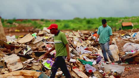 Two-men-in-dirty-clothes-search-through-a-pile-of-garbage-at-a-city-garbage-dump-in-Brazil