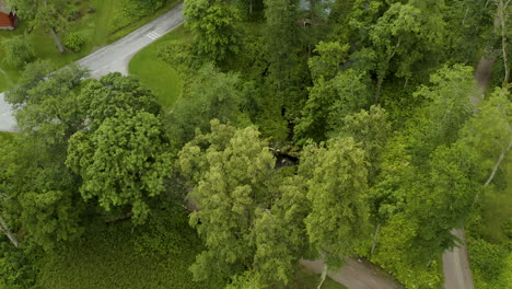 Aerial-view-away-from-a-small-waterfall-revealing-the-Fagervik-town,-overcast,-summer-day,-in-Inkoo,-Finland---reverse,-tilt-up,-drone-shot