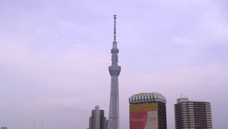 Statische-Ansicht-Von-Tokio-Skytree-Mit-Flugzeug,-Das-Mit-Hintergrund-Auf-Blauem-Bewölktem-Himmel-Fliegt