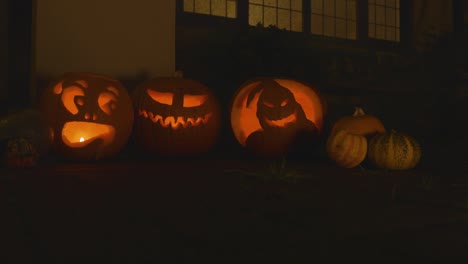 3-carved-lit-pumpkins-outside-the-front-of-a-house-Halloween-with-smoke-and-small-pumpkins