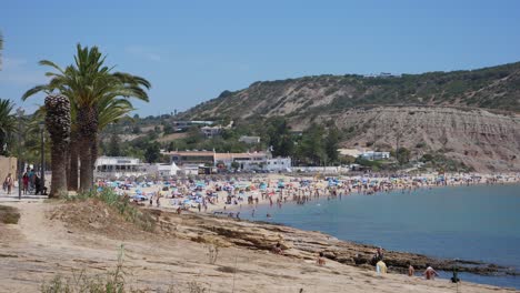 Establecimiento-De-Tiro,-Gente-Caminando-En-La-Costa-Rocosa-En-Algarve,-Portugal,-Vista-Panorámica-De-La-Gente-Disfrutando-De-La-Playa-De-Arena-En-Un-Día-Soleado