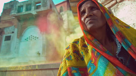 A-woman-wears-a-colorful-scarf-covering-her-head-as-she-sits-outside-and-colorful-chalk-dust-flies-behind-her