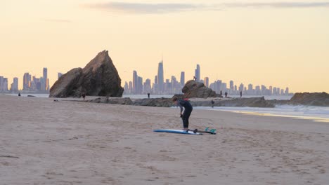 Surfer-Im-Neoprenanzug,-Der-Das-Surfbrett-In-Der-Currumbin-Alley-Während-Des-Sonnenuntergangs-Wechselt---Surfers-Paradies-Wolkenkratzer-Im-Hintergrund---Gold-Coast,-Queensland,-Australien