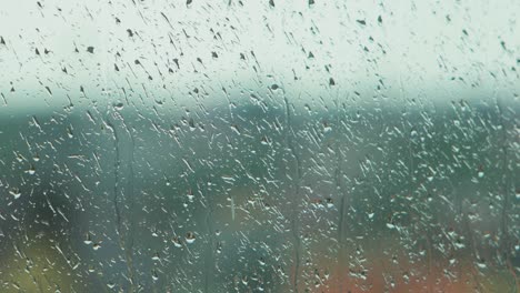Rain-drops-sliding-slow-on-window-glass-in-rainy-day,-medium-closeup-shot