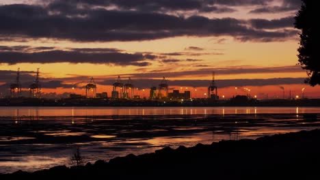 Illuminated-Cranes-At-The-Port-Of-Tauranga-Across-Tauranga-Harbour-In-New-Zealand-During-Sunset---Golden-Hour---wide-shot,-zoom-in