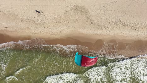 AERIAL:-Top-View-Shot-of-Surfer-Stranded-on-Sandy-Beach-with-Crashing-Waves