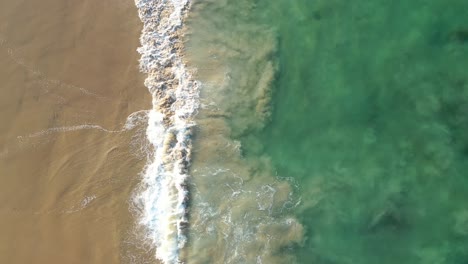 Ariel-drone-shot-of-crystal-clear-water-and-waves-crashing-into-the-sand-on-a-stunning-sunny-day-along-the-California-coastline
