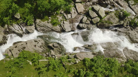 Birds-eye-aerial-shot-of-a-stream-flowing-down-the-rocks-in-a-grassy-Norwegian-countryside