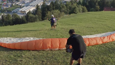 Videographer-films-tandem-paragliders-launching.-Slovenj-Gradec,-Slovenia