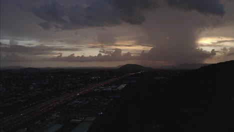 Aerial-shot-of-a-highway-leading-to-a-hill-with-a-lightning-strike-on-the-horizon