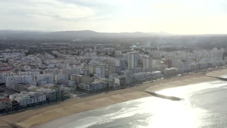 Quarteira-beach-lined-with-tall-white-hotels-and-residential-beachside-luxury-buildings,-Drone-Aerial-Portugal