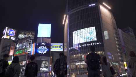 Low-angle-view-of-people-waiting-at-famous-Shibuya-Scramble-in-Tokyo,-Japan-during-night-with-adverts-in-background