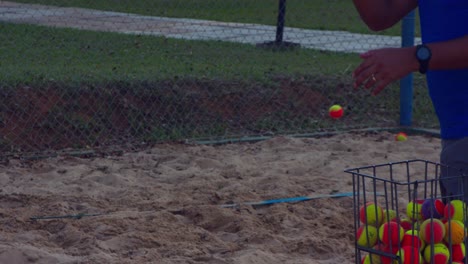 Man-hitting-tennis-balls-over-the-net-for-a-play-practicing-to-volley-back-in-Beach-Tennis