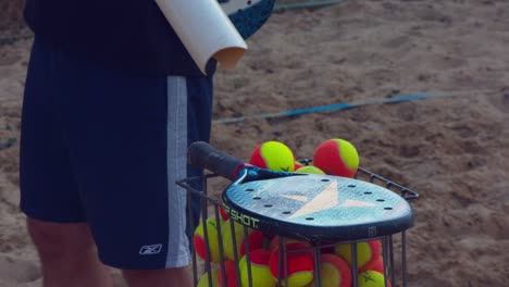 Man-using-a-tube-full-of-beach-tennis-balls-to-fill-a-basket-for-practice-session