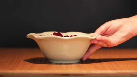 Person's-Hand-Served-The-Bowl-Of-Mixed-Berries-With-Oats-On-A-Wooden-Table