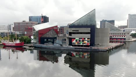 Aerial-pan-over-Patapso-River-at-Inner-Harbor,-Chesapeake-Bay,-National-Aquarium,-submarine,-Top-of-the-World-observation-tower,-reflections-in-water