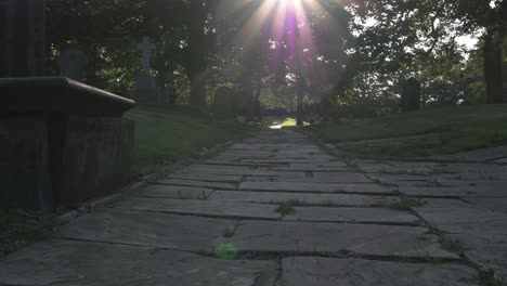 Sunbeams-over-old-Churchyard-pathway-at-sunset-wide-panning-shot