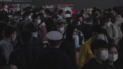 Un-Policía-Con-Máscaras-Que-Realiza-Una-Vigilancia-Con-La-Multitud-Que-Pasa-Por-La-Estación-De-Shibuya-En-La-Noche-De-Halloween-En-Tokio,-Japón---Cámara-Lenta-De-Tiro-Medio