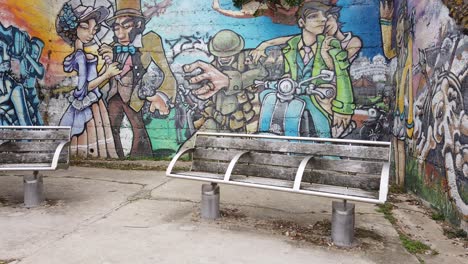 Hand-held-footage-of-shabby-bench-with-wall-mural-in-background-handheld