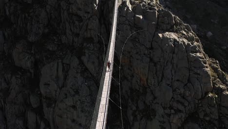 A-slow-tilting-up-shot-of-a-single,-young-man-walking-confidently-alone-in-the-outdoors-over-a-suspension-bridge-in-Trifthutte,-Switzerland