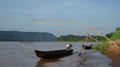 Long-Boat-crossing-the-Mekong-River-from-Thailand-to-Laos-side-while-two-other-boats-bouncing-on-muddy-brown-water-while-moored-at-the-Thai-river-bank-in-Huai-Phai,-Ubon-Ratchathani