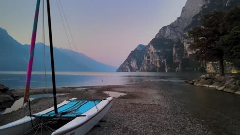 Lake-Garda-at-sunrise-aerial-panorama,-boat,-mountains,-romantic-morning-light