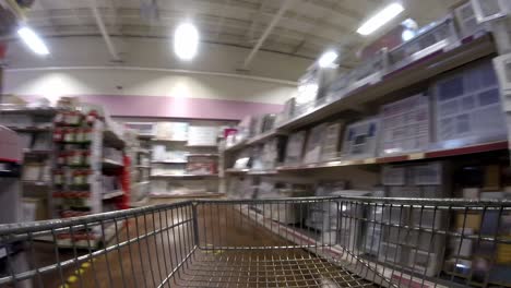 Retail-shopping-cart-moving-down-variety-of-merchandise-aisle-in-shopping-mall-during-covid-pandemic
