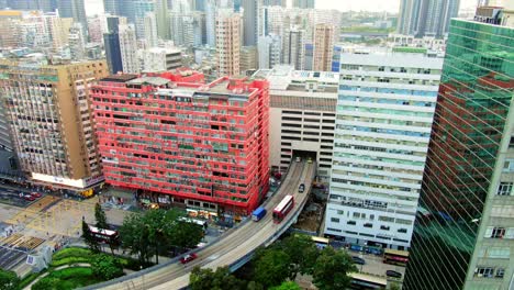 Traffic-passing-through-a-Car-park-building-in-downtown-Hong-Kong,-with-city-mega-buildings,-Aerial-view