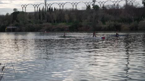 Four-people-paddle-in-standing-kayaks-on-river-rippling-with-cool-evening-light