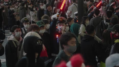 Policías-Con-Máscaras-Con-Luces-Rojas-De-Bastón-De-Tráfico-Dando-Señales-A-La-Multitud-Ocupada-En-La-Noche-De-Halloween-En-El-Cruce-De-Shibuya-En-Tokio,-Japón---Cámara-Lenta