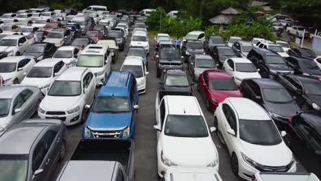 AERIAL:-Drone-travels-low-Above-the-Packed-Parking-Zone-with-hundreds-of-Cars,-People-Wait-in-Queue-to-be-Transported-by-Ferry-from-The-Koh-Chang-Island-to-Mainland-of-Trat,-Thailand,-Asia