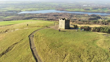 Tourists-on-summit-of-Rivington-tower-Lancashire-reservoir-countryside-aerial-view-pull-away-orbit-right