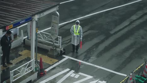 Traffic-Enforcer-In-Raincoat-And-Safety-Vest-Working-Under-The-Rain-On-The-Road-In-Shibuya,-Tokyo---high-angle-shot