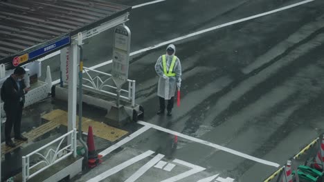 Ejecutor-De-Tráfico-En-Impermeable-Y-Chaleco-De-Seguridad-Trabajando-Bajo-La-Lluvia-En-La-Carretera-En-Shibuya,-Tokio---Tiro-De-ángulo-Alto