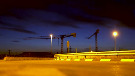 Cars-speed-down-the-road-with-two-construction-cranes-at-the-bottom-of-the-box-and-as-dusk-falls