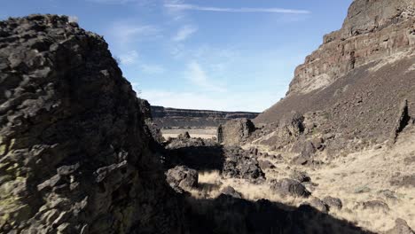 Skimming-ancient-basalt-volcanic-columns-on-the-canyon-floor-of-Dry-Falls-State-Park,-aerial