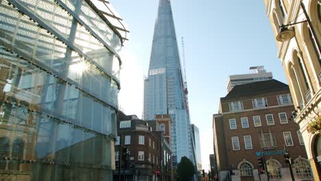 Cinematic-slow-motion-pan-up-revealing-The-Shard-skyscraper-in-summer-sunlight-with-sun-stars-and-blue-skies