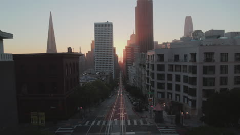 An-aerial-view-down-a-road-in-a-city-at-dawn-with-the-camera-backing-away-further-down-the-road