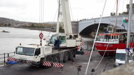 Hydraulic-crane-vehicle-loading-fishing-boat-on-Conwy-Wales-harbour