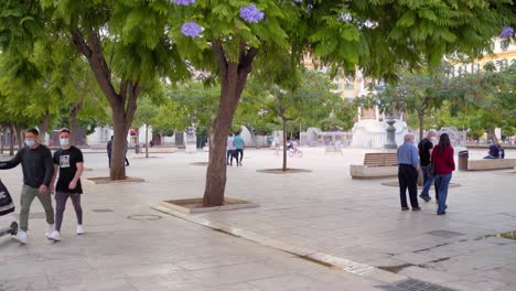 Gente-Paseando-En-La-Plaza-De-La-Merced-Durante-La-Pandemia-De-Covid-19-En-Málaga,-España---Usando-Máscaras-Para-Protegerse---Plano-General