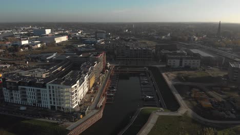 Aerial-approach-of-construction-site-of-the-new-Noorderhaven-neighbourhood-and-river-IJssel-that-flows-passed-Hanseatic-Dutch-city-of-Zutphen-on-a-hazy-morning-against-a-blue-sky