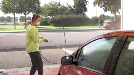 Woman-cleaning-hood-of-a-red-car-with-pressure-hose-and-matching-sweatshirt-with-green-hair-and-background