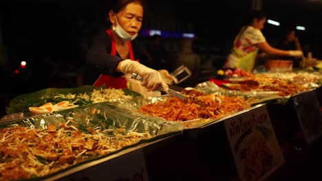Asian-Street-Food---Thai-Saleswoman-behind-the-counter-puts-food-to-the-buyer
